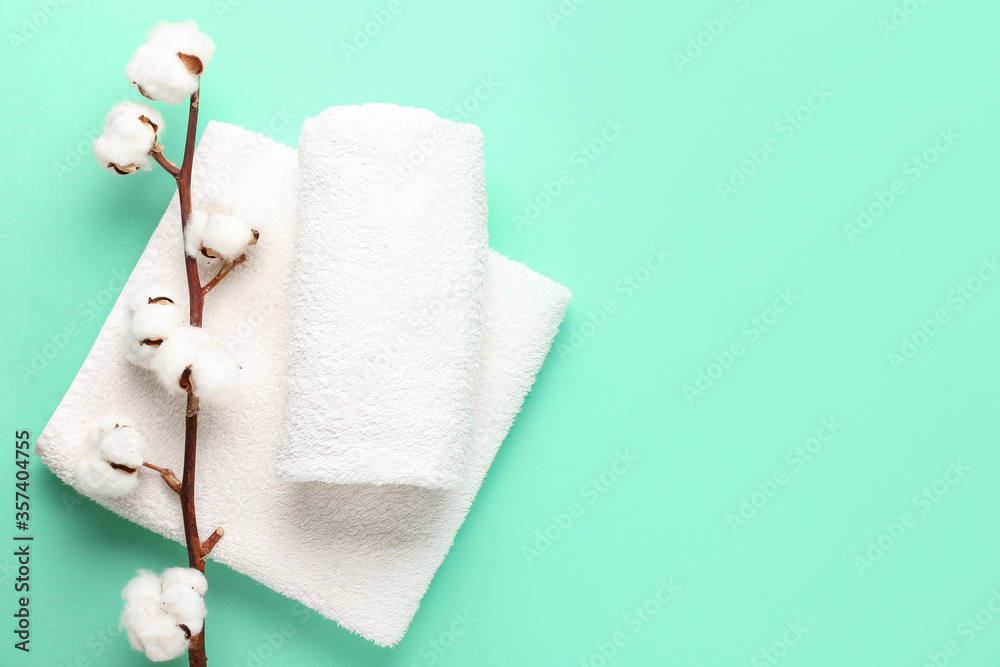 Cotton flowers and soft towels on color background