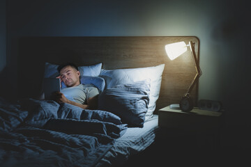 Wall Mural - Young man suffering from sleep deprivation with tablet computer in bedroom at night