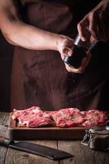 Wall Mural - Man cooking meat steaks on kitchen. Chef salt and pepper meat on wooden background