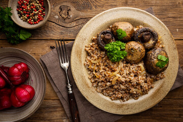 Wall Mural - Buckwheat porridge with mushrooms in a plate on wooden table, top view