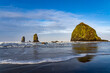 Haystack Rock and the Needles reflected in the wet sand, with wave foam and blue sky and clouds, Canon Beach, Oregon