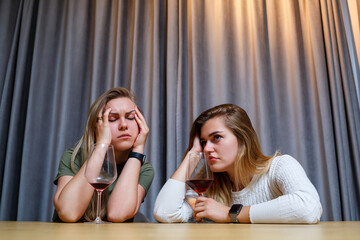 A woman consoles a sad depressed friend who needs help. Depression with alcohol concept. upset young girl with unhappy face holding a glass of wine looking at her best sister