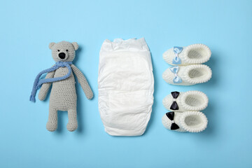 Wall Mural - diaper, toy bear and booties on light blue background, flat lay