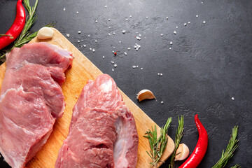 Wall Mural - raw meat on a kitchen Board with garlic  and red chili pepper on a black background top view, pork,