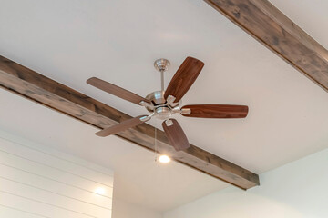 Ceiling fan with lights between decorative wood beams inside living room of home