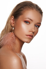 Fashion vogue style closeup beauty face portrait of young beautiful blonde woman with perfect makeup and feather earrings posing against white background