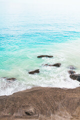 Blue sea water surface and soft wave on the dark sand. Tropical beach background, top view