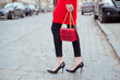 Fashion woman with red snake print handbag on the city street . Street style . She is wearing knit sweater and high heels.