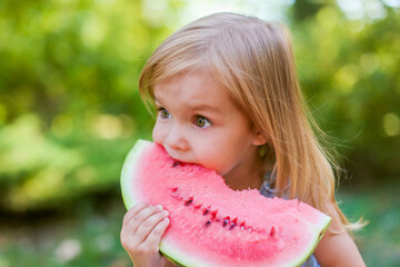 Child eating watermelon in the garden. Kids eat fruit outdoors. Healthy snack for children. 2 years old girl enjoying watermelon.