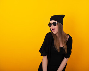 Leinwandbilder - Stylish girl with sunglasses over yellow background. Studio female portrait. Happy charming woman wearing black clothes posing indoor