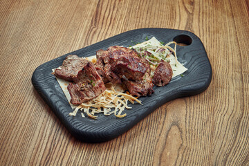 Yummy beef kebab with lavash and onions on a black tray on a wooden background. Barbecue. Meat cooked on the grill