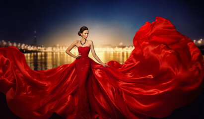 fashion model in fluttering dress in night city street lights, elegant woman in red long gown, full 