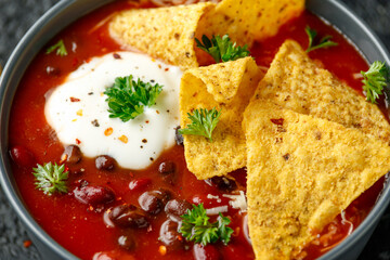 Mexican Chilli bean soup with yogurt, cheese and tortilla chips in black bowl