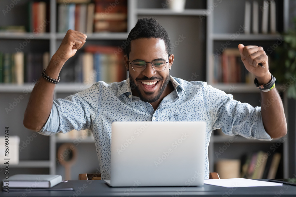 African guy feels happy received great news by internet looks at pc screen raised hands scream with joy celebrating on-line lottery win, successful admission to college, offers big discounts concept - obrazy, fototapety, plakaty 