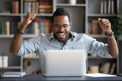 Fotografía African guy feels happy received great news by internet looks at pc screen raise
