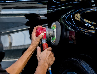 The worker polishes a car with the electric tool.