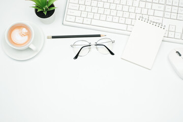 Flat lay business office concept on modern white table desk background with blank notepad and keyboard computer, mouse and eyeglasses, green plant and coffee cup,Top view with copy space