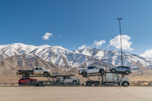 Car Carrier Truck With New Pick-up Trucks And Snow-covered Mountains In Background
