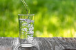 Water is poured into a glass against a background of greenery. A glass of water on a hot summer day with space to copy.