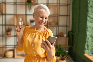 technology, aging and gadgets concept. attractive cheerful female pensioner in yellow dress using mo