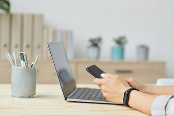 Wall Mural - Side view close up of unrecognizable young woman holding smartphone over laptop while working at home office, copy space