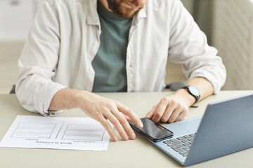 Cropped portrait of bearded young man using smartphone while working at home office in minimal light interior, copy space