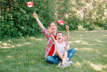 Family Mom With Son Celebrating National Canada Day On 1st Of July. Caucasian Mother With Child Boy Waving Canadian Flags. Proud Citizens Celebrate Canada Day In Park Outdoors.