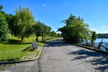 Park pathway with benches, lake, trees and grass in Staten Island, NY