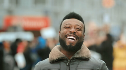 Close-up young adult American black man in jacket smiling and looking at camera. Smile human. Cold winter in New York. Happy african people in city on street closeup look. Male laughing. White teeth.