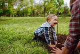 Fototapeta Dmuchawce - Little boy helping his grandfather to plant the tree while working together in the garden. Fun little gardener. Spring concept, nature and care.
