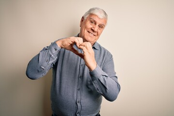 Wall Mural - Senior handsome hoary man wearing casual shirt standing over isolated white background smiling in love doing heart symbol shape with hands. Romantic concept.