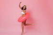 © Look! - Pleased girl in bikini jumping on pink background. Studio shot of excited young woman with swimming circle.