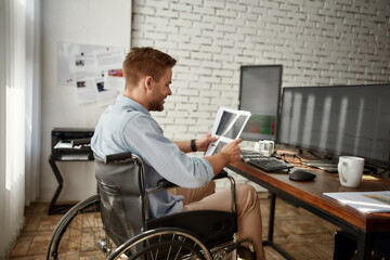 Successful trader. Young male businessman in a wheelchair analyzing stock graph report and smiling while working at his workplace in the modern office