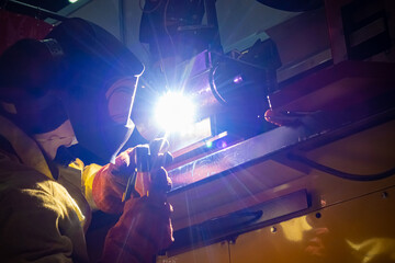 Poster - Hot welding. Welder in the process. A man in a protective helmet works with welding. Concept - work as a welder. Connection of metal parts. Concept - sale of welding equipment.