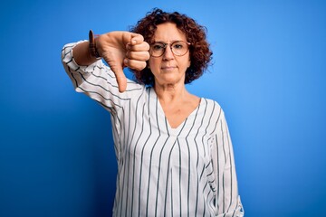 Wall Mural - Middle age beautiful curly hair woman wearing casual striped shirt over isolated background looking unhappy and angry showing rejection and negative with thumbs down gesture. Bad expression.