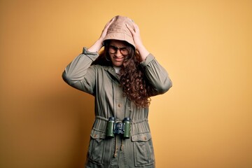 Poster - Young beautiful tourist woman on vacation wearing explorer hat and binoculars suffering from headache desperate and stressed because pain and migraine. Hands on head.