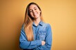 © Krakenimages.com - Young beautiful blonde woman with blue eyes wearing denim shirt over yellow background happy face smiling with crossed arms looking at the camera. Positive person.
