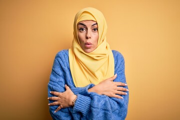 Sticker - Young beautiful brunette muslim woman wearing arab hijab over isolated yellow background shaking and freezing for winter cold with sad and shock expression on face