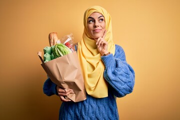 Canvas Print - Young beautiful brunette arab woman wearing islamic hijab holding paper bag with food serious face thinking about question, very confused idea