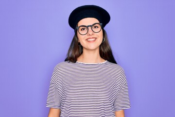 Poster - Young beautiful brunette woman wearing glasses and french beret over purple background with a happy and cool smile on face. Lucky person.