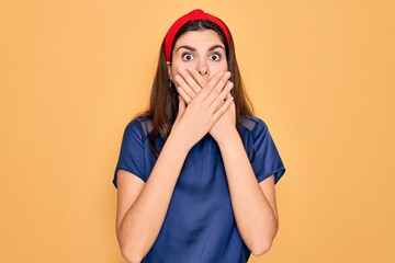 Poster - Young beautiful brunette woman wearing red lips over yellow background shocked covering mouth with hands for mistake. Secret concept.