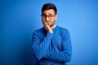 © Krakenimages.com - Young handsome man with beard wearing casual sweater and glasses over blue background thinking looking tired and bored with depression problems with crossed arms.