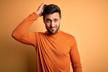 Wall Mural - Young handsome man with beard wearing casual sweater standing over yellow background confuse and wonder about question. Uncertain with doubt, thinking with hand on head. Pensive concept.