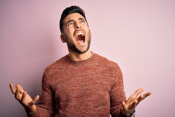 Sticker - Young handsome man wearing casual sweater standing over isolated pink background crazy and mad shouting and yelling with aggressive expression and arms raised. Frustration concept.