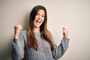 Sticker - Young beautiful girl wearing casual sweater standing over isolated white background celebrating surprised and amazed for success with arms raised and open eyes. Winner concept.