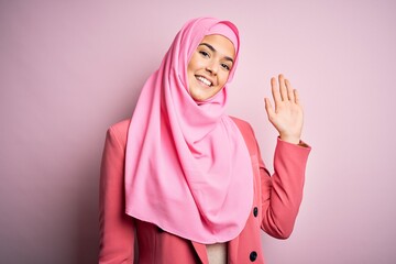 Sticker - Young beautiful girl wearing muslim hijab standing over isolated pink background Waiving saying hello happy and smiling, friendly welcome gesture