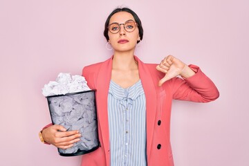 Wall Mural - Young beautiful business woman with blue eyes holding heap bin of crumpled papers with angry face, negative sign showing dislike with thumbs down, rejection concept