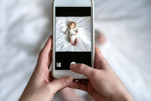 Above High Angle Shot Of Happy Mom Taking Photo Her Baby Boy Or Girl In Bed With A Smartphone At Home. It Is A Memorable Feeling For Every Parent When Their Child Is Growing Up. Top View