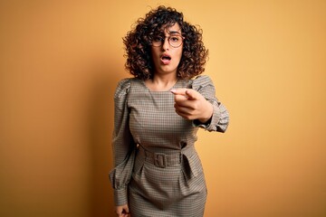 Poster - Beautiful arab business woman wearing dress and glasses standing over yellow background pointing displeased and frustrated to the camera, angry and furious with you