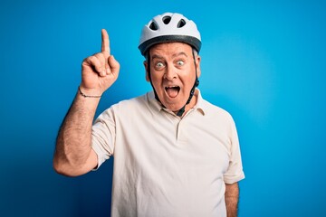 Wall Mural - Middle age hoary cyclist man wearing bike security helmet over isolated blue background pointing finger up with successful idea. Exited and happy. Number one.